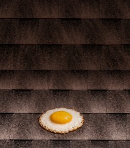 Fried egg cooking on a hot asphalt shingle roof illustrating how summer heat increases roof temperatures and energy costs.
